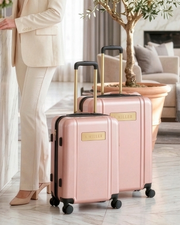 Vaaleanpunainen matkalaukku ja käsimatkatavaralaukku, joissa on kaiverrettu nimi