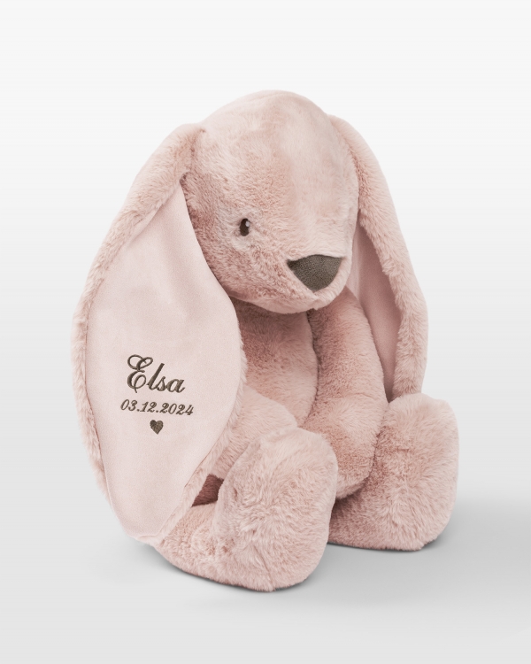 Iso pupu pehmolelu ruskealla kirjonnalla ja nimi sekä syntymäaika.