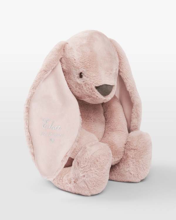 Iso pupu pehmolelu valkoisella kirjonnalla ja nimi sekä syntymäaika.