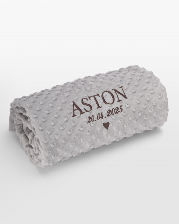 Harmaa vauvanpeitto nimellä ruskealla brodeerauksella