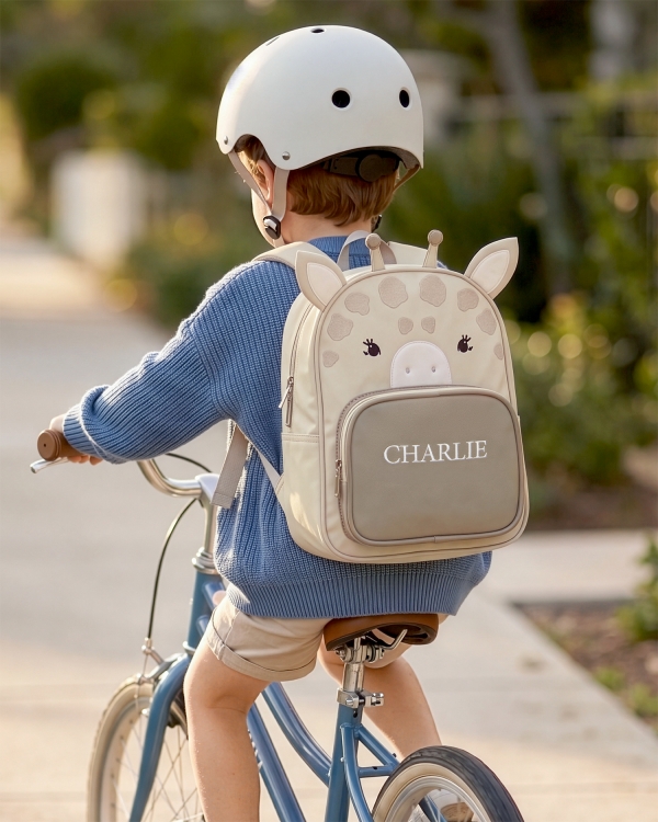 Lasten beige kirahvireppu valkoisella nimellä pojan selässä
