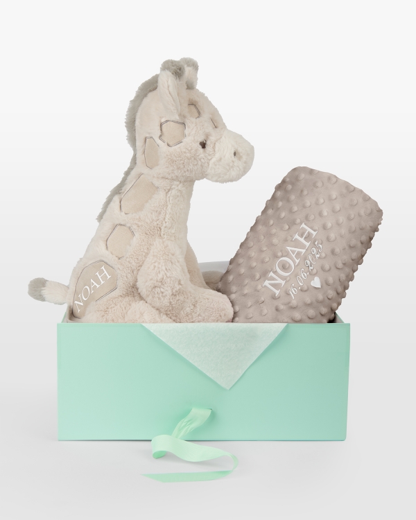 Pehmolelu ja ruskea peitto, jossa kirjailtu nimi ja päivämäärä