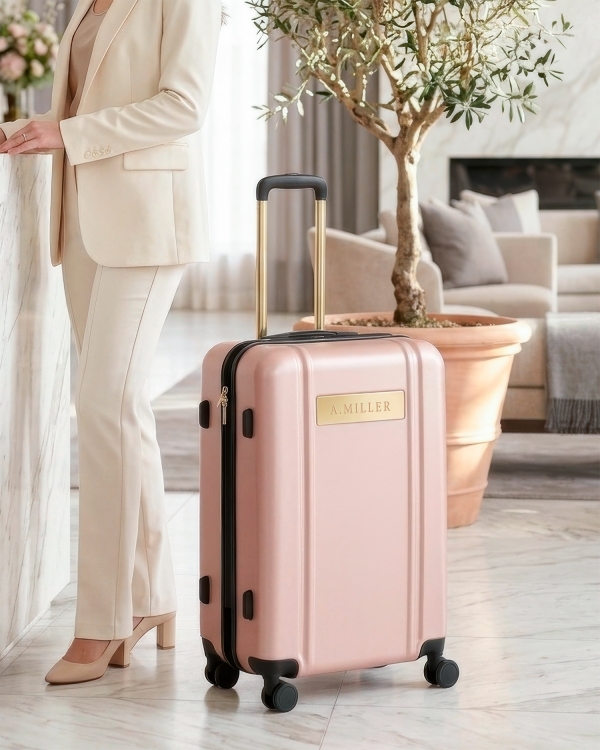 Vaaleanpunainen matkalaukku kultavärisillä yksityiskohdilla ja nimellä