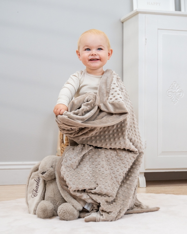 Hiekanvärinen vauvan viltti, jossa on nimikirjonta.