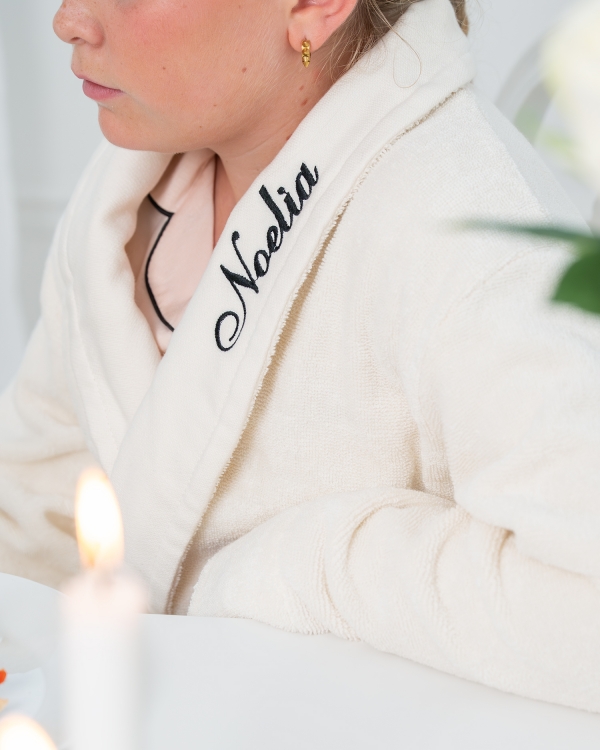 Ylellinen kermanvärinen kylpytakki, jossa musta kirjailtu nimi lapsille