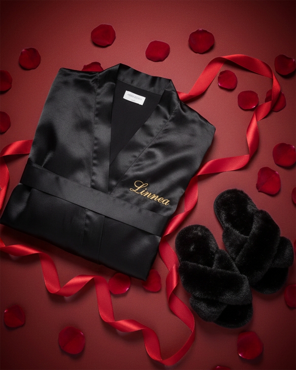 Mukava ystävänpäivälahja hänelle, jossa on mustat pehmeät tohvelit ja musta satiinikylpytakki, johon on kirjailtu nimi kultaisel